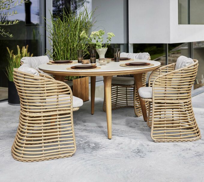 Der runde Aspect Tisch mit Fossil-Keramikplatte im Travertine look mit Basket Sesseln mit hellbraunen Wove-Kissen, alles von Cane-line.
