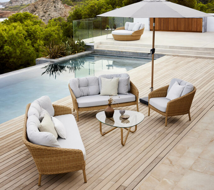 Ocean Large Lounge mit Daybed im Hintergrund dazu ein Wave-Tisch und ein Sunshade-Sonnenschirm, alles von Cane-line.