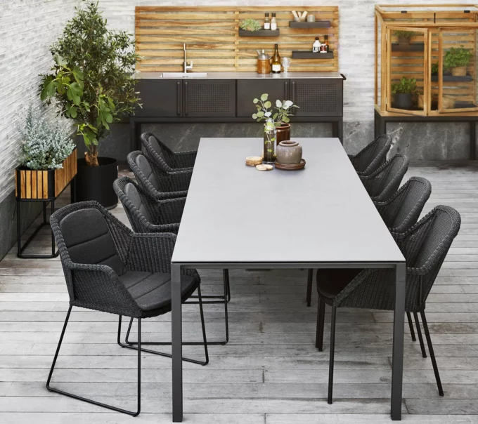 Von Cane-line schwarze Breeze-Sessel mit Kufen am lavagrauen Pure-Tisch mit Concrete grey Keramikplatte.